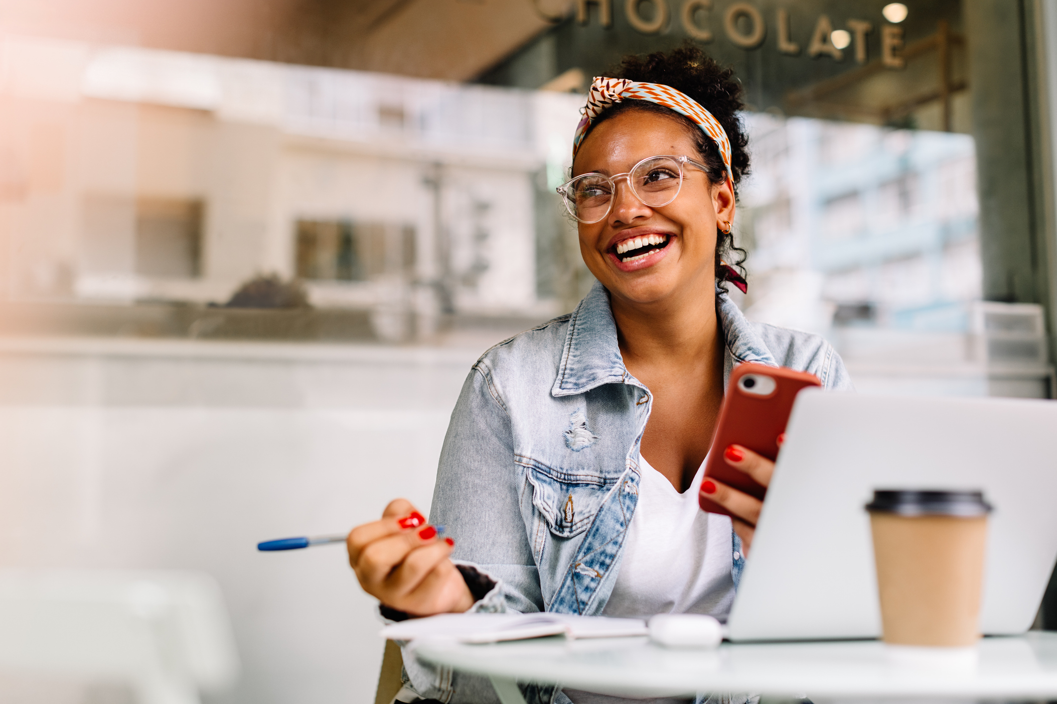 Woman Looking At Her Phone And Laptop With Pen In Hand